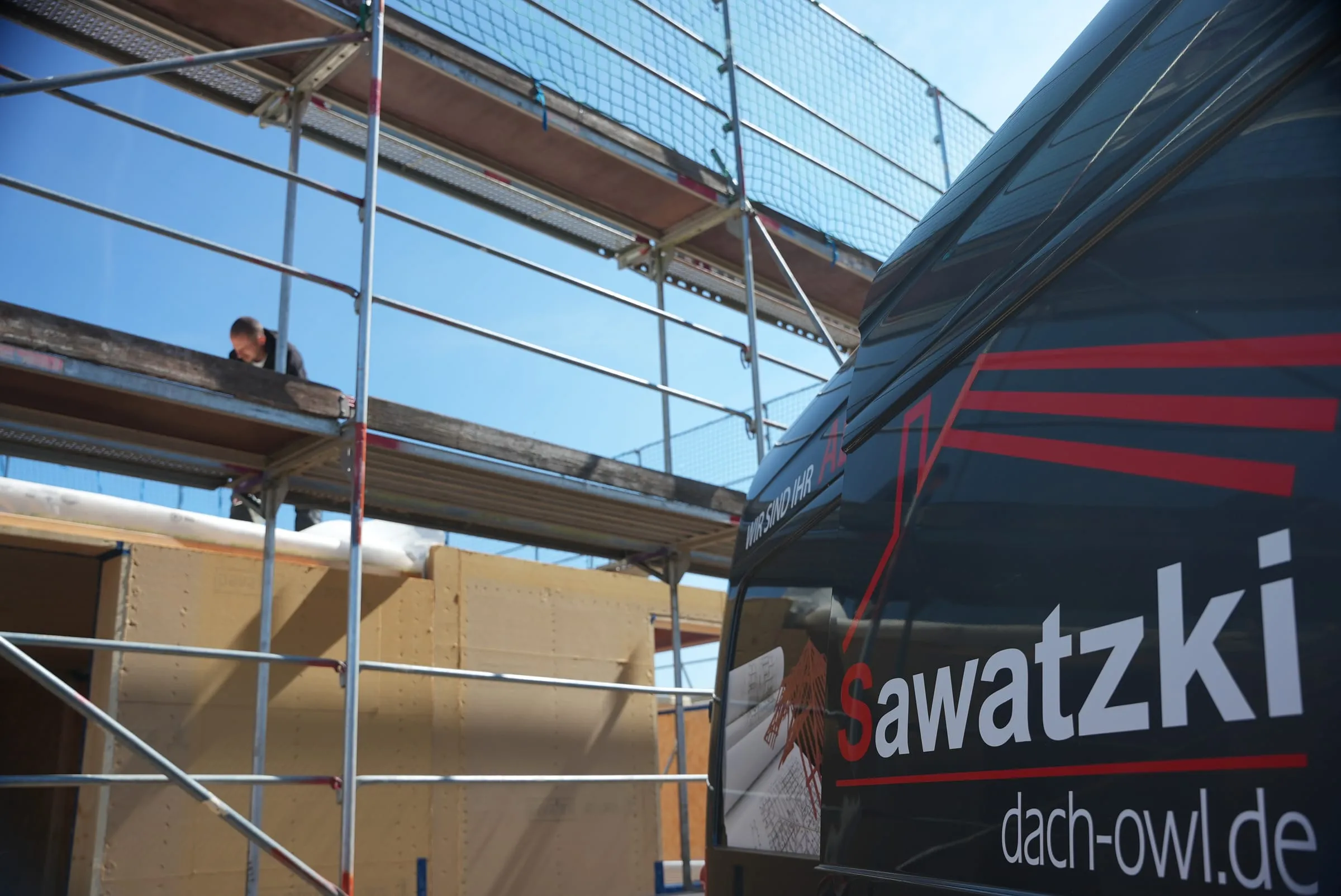 Sawatzki-Transporter mit Firmenschriftzug an einer eingerüsteten Holzbau-Baustelle in OWL